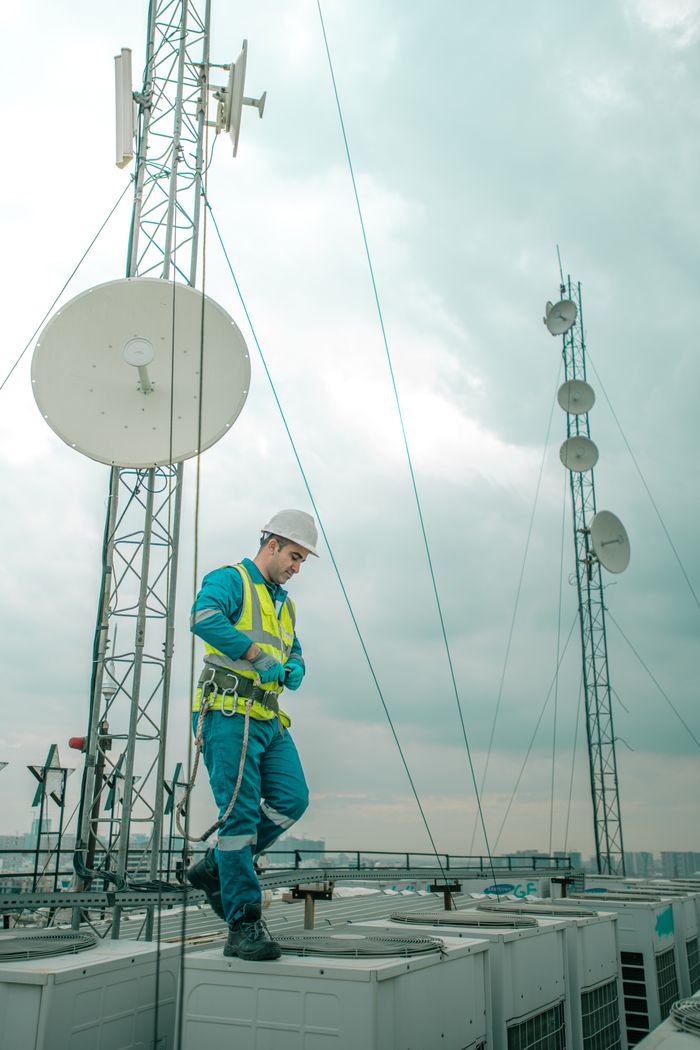 services-03 Telecommunications worker in Shaqlawa adjusting equipment on rooftop, wearing safety gear.