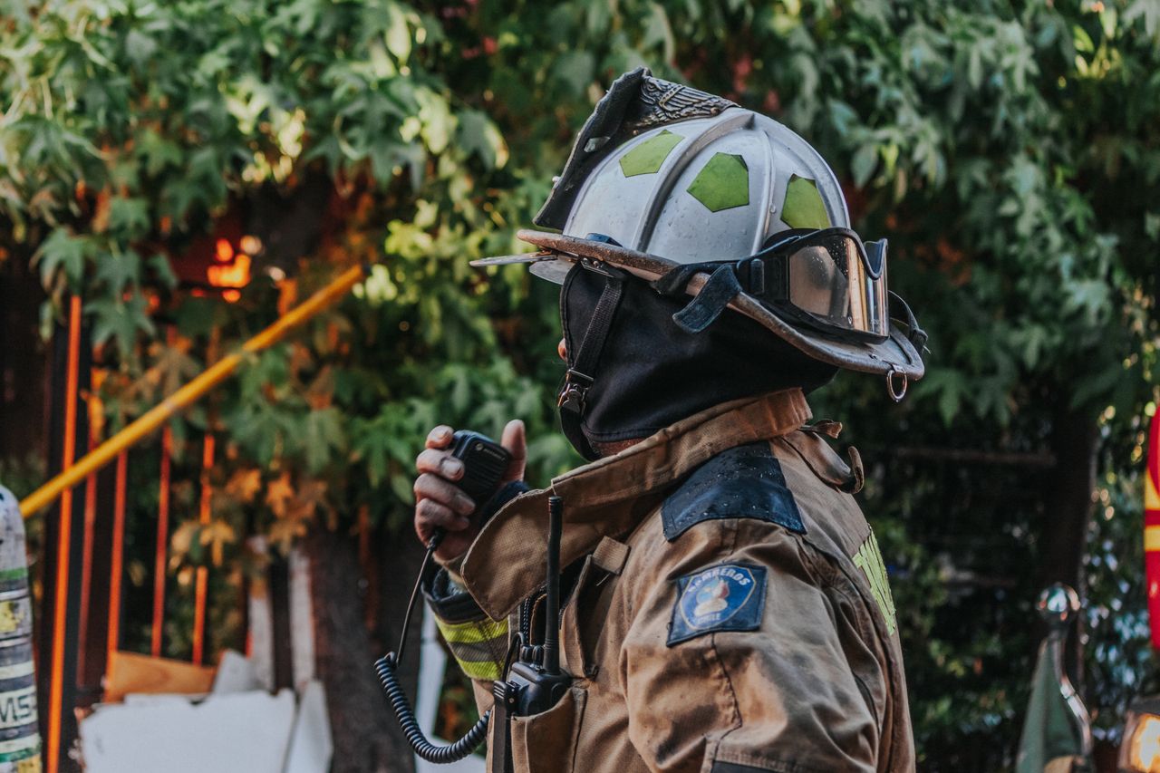 services-04 Firefighter in full protective gear using a radio outdoors.