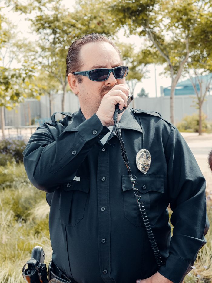 team-03 Police officer in uniform using a radio outdoors on a sunny day.